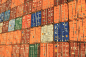 A tightly stacked wall of colorful shipping containers in various shades of orange, blue, red, green, and white, representing global freight transport and logistics.