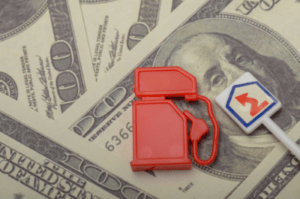 pile of cash with a fuel pump toy and windy road sign.