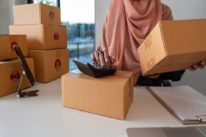 businesswoman-with-boxes-using-calculator-at-desk